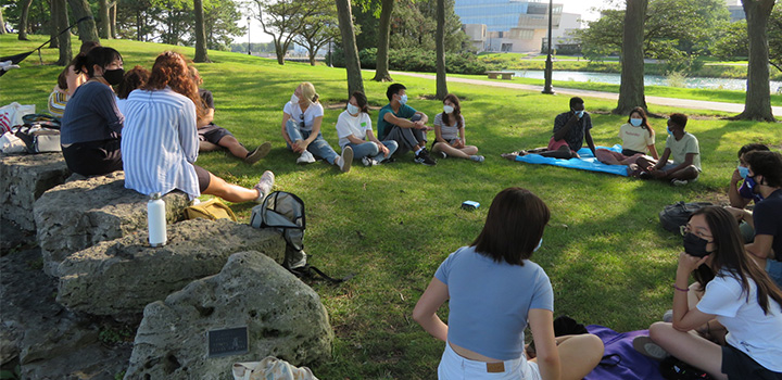 students sitting outside together in the grass on campus